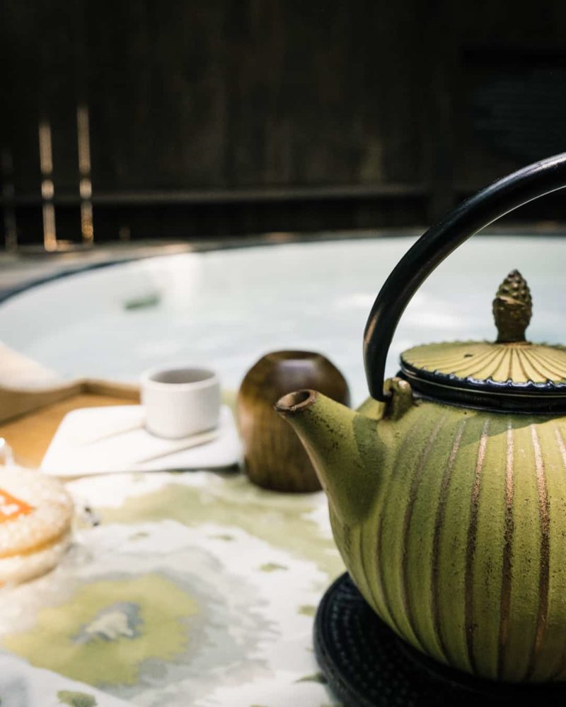 a tea kettle, cups, and pastries on a tray and a hot tub in the background